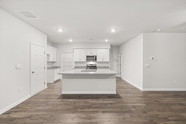 kitchen with white cabinetry, dark wood-type flooring, light stone counters, a center island with sink, and appliances with stainless steel finishes