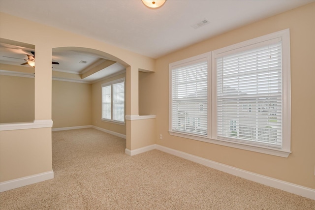 carpeted spare room featuring arched walkways, ceiling fan, baseboards, and a tray ceiling