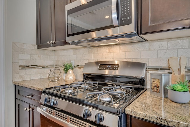 kitchen featuring stainless steel appliances, dark brown cabinets, tasteful backsplash, and light stone counters