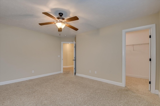 unfurnished bedroom with light carpet, a walk in closet, and baseboards