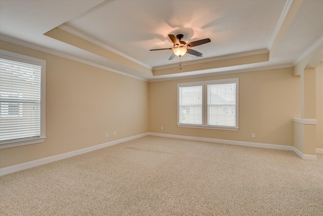 empty room featuring a raised ceiling, crown molding, a ceiling fan, carpet, and baseboards