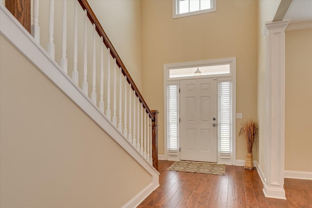entryway with wood-type flooring, a high ceiling, ornate columns, baseboards, and stairs