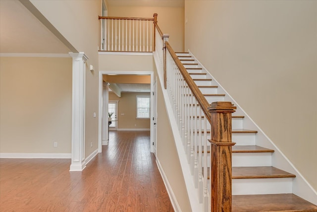 staircase with hardwood / wood-style flooring, baseboards, a high ceiling, and ornate columns