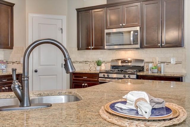 kitchen featuring stainless steel appliances, a sink, dark brown cabinets, and tasteful backsplash
