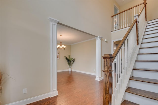 stairs featuring wood finished floors, a chandelier, baseboards, decorative columns, and crown molding