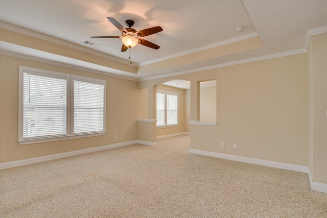 empty room featuring a ceiling fan, arched walkways, light colored carpet, crown molding, and a raised ceiling