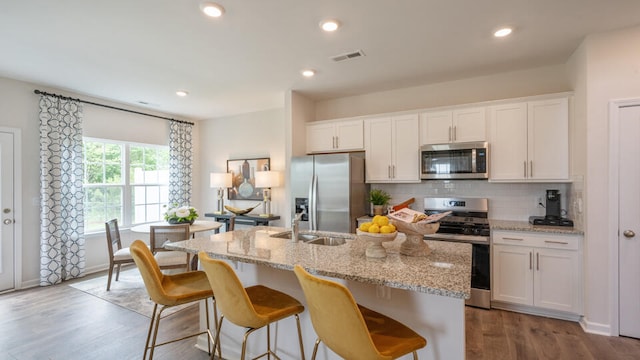 kitchen featuring appliances with stainless steel finishes, white cabinets, an island with sink, and tasteful backsplash