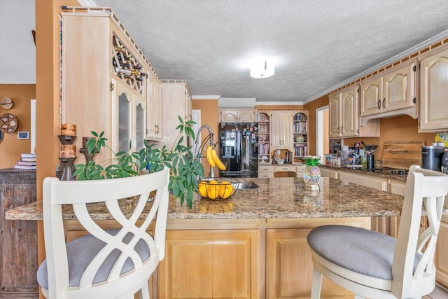 3974 Bolton St, Augusta, GA 30909 - kitchen featuring black appliances, a breakfast bar area, light stone countertops, light brown cabinets, and a textured ceiling