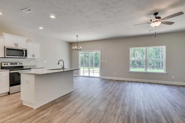 kitchen featuring a center island with sink, ceiling fan with notable chandelier, appliances with stainless steel finishes, decorative light fixtures, and white cabinetry