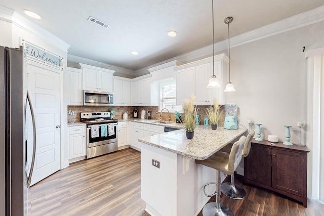 kitchen with white cabinets, appliances with stainless steel finishes, decorative light fixtures, kitchen peninsula, and a breakfast bar area