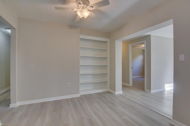 interior space with a ceiling fan, built in shelves, baseboards, and wood finished floors