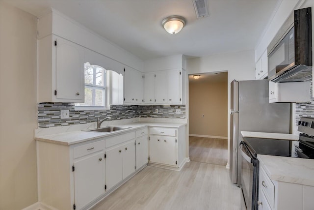 kitchen featuring black microwave, a sink, backsplash, stainless steel electric range oven, and light wood finished floors