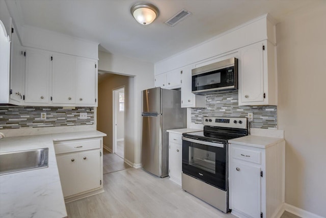 kitchen with a sink, visible vents, white cabinetry, light countertops, and appliances with stainless steel finishes