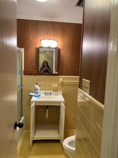 bathroom with crown molding, sink, tile walls, and toilet