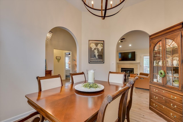 267 Fairway Dr, Mccormick, SC 29835 - dining room featuring arched walkways, a high ceiling, a chandelier, a fireplace, and light wood-style flooring
