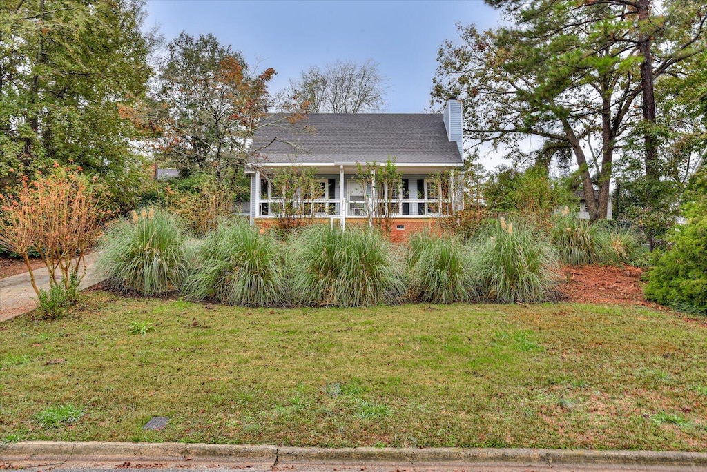 view of front facade with a front yard, covered porch, and a chimney