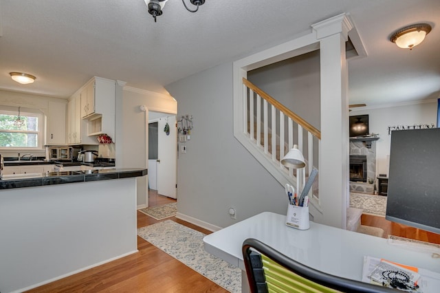 1414 Brookgreen Dr, North Augusta, SC 29841 - kitchen with dark countertops, light wood-style flooring, white cabinetry, crown molding, and a tiled fireplace