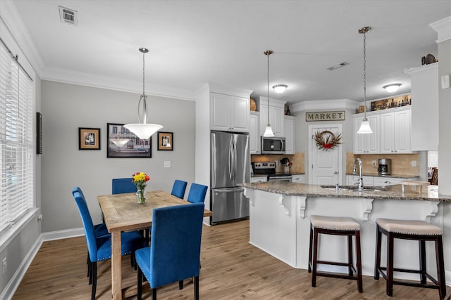 kitchen featuring pendant lighting, appliances with stainless steel finishes, white cabinets, a sink, and dark stone countertops