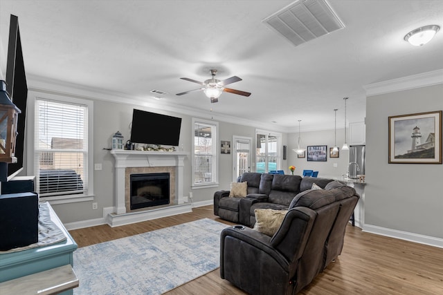 living area with light wood-type flooring, a healthy amount of sunlight, visible vents, and crown molding