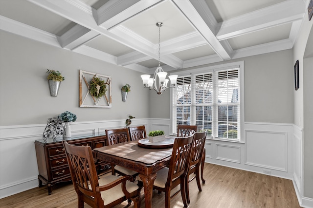 dining area with coffered ceiling, a wainscoted wall, light wood-style flooring, an inviting chandelier, and beam ceiling