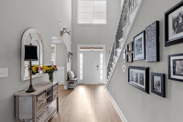 foyer entrance featuring visible vents, stairway, a high ceiling, light wood-style floors, and baseboards