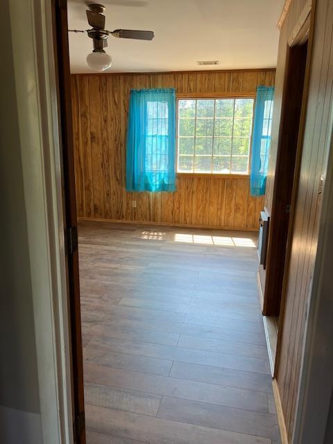 empty room with wood-type flooring, a ceiling fan, wood walls, and visible vents