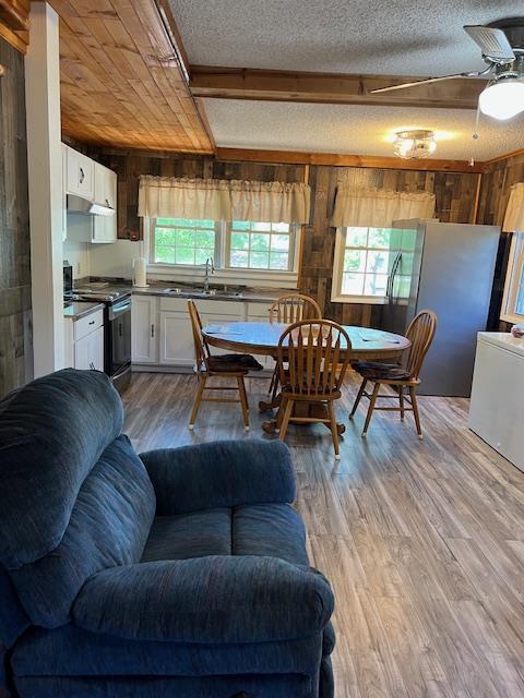 dining space with ceiling fan, wooden walls, light wood-type flooring, a textured ceiling, and wood ceiling