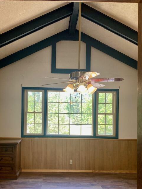 empty room with lofted ceiling with beams, wainscoting, a ceiling fan, and wood finished floors