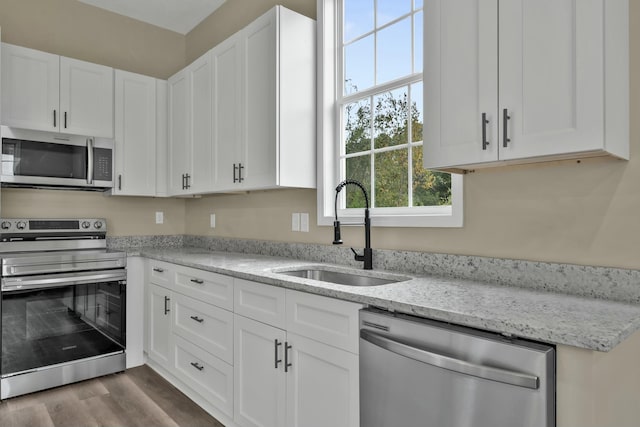 kitchen with white cabinets, appliances with stainless steel finishes, light stone counters, and sink