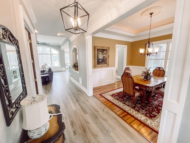 dining space with a chandelier, a decorative wall, ornamental molding, light wood-type flooring, and wainscoting