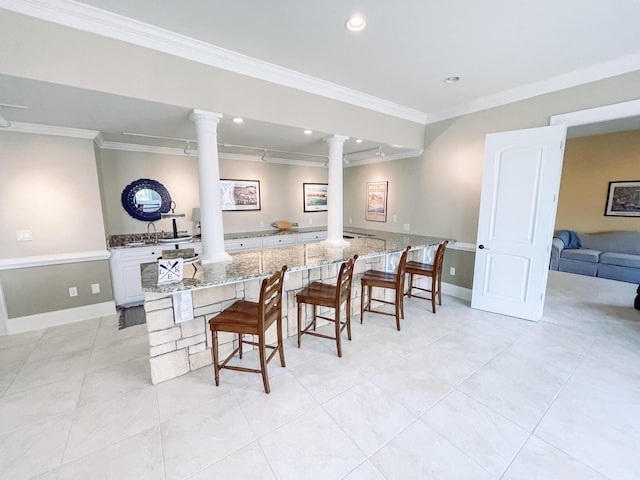 kitchen featuring ornamental molding, light stone counters, decorative columns, and a kitchen breakfast bar