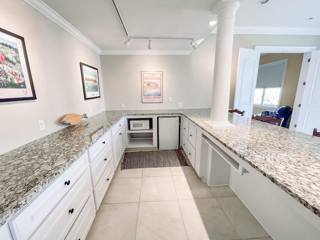 kitchen with a peninsula, light stone counters, white cabinetry, and ornate columns