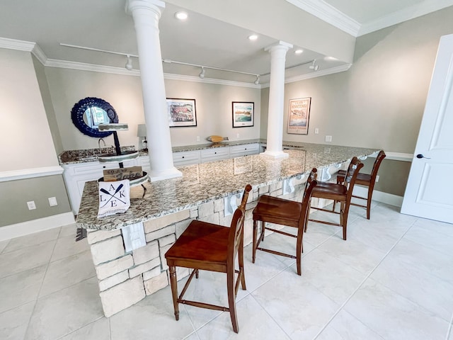 kitchen with a peninsula, a breakfast bar area, decorative columns, and white cabinets