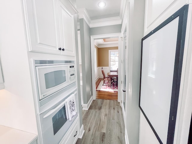 kitchen with light wood finished floors, white cabinets, white microwave, a wainscoted wall, and ornamental molding