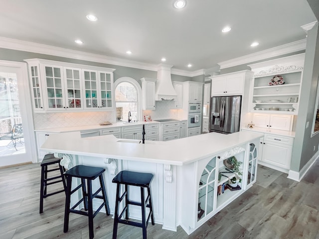 kitchen featuring a spacious island, light countertops, stainless steel fridge with ice dispenser, open shelves, and custom range hood