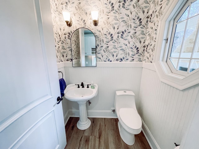 half bath featuring wainscoting, wood finished floors, toilet, and wallpapered walls