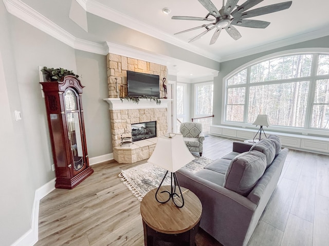 living room featuring a stone fireplace, ornamental molding, light wood-style flooring, and baseboards