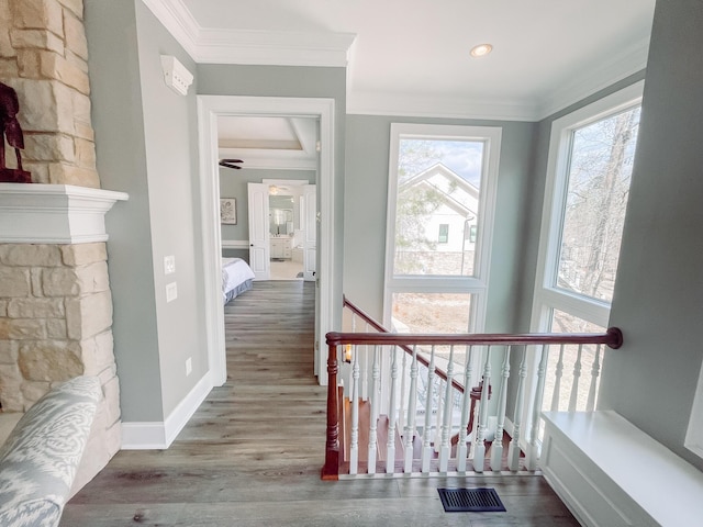 corridor with visible vents, wood finished floors, crown molding, and an upstairs landing