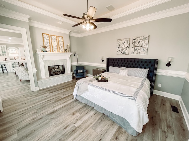 bedroom featuring a fireplace, visible vents, ornamental molding, wood finished floors, and baseboards