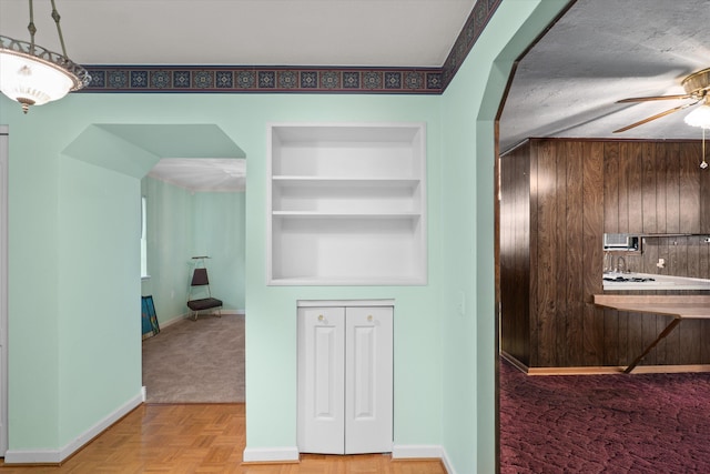 kitchen with parquet floors, wooden walls, built in shelves, ceiling fan, and a textured ceiling