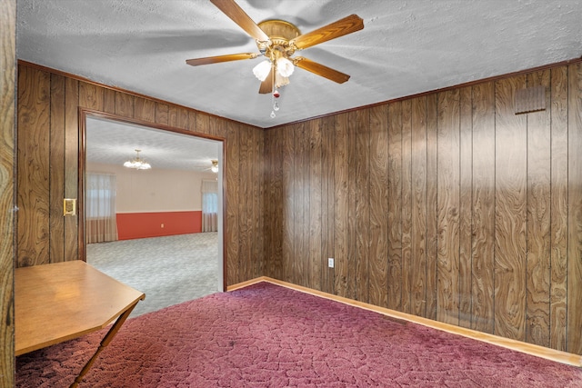 carpeted empty room with wood walls, ceiling fan with notable chandelier, and a textured ceiling