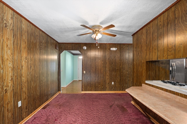 unfurnished living room featuring carpet, wooden walls, ceiling fan, ornamental molding, and a textured ceiling