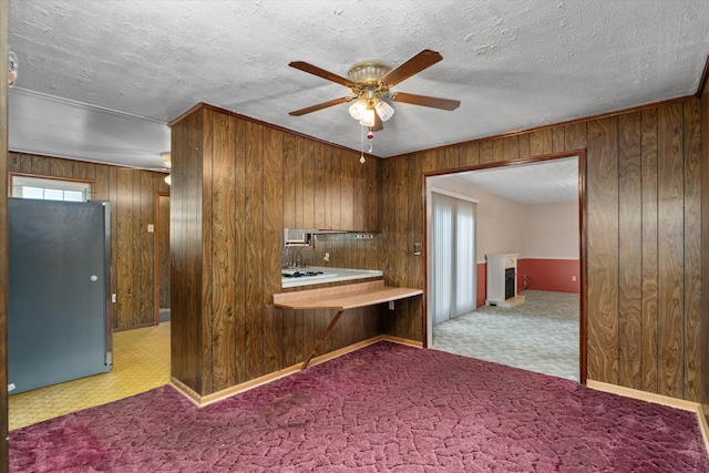 kitchen featuring wooden walls, ceiling fan, light carpet, and stainless steel refrigerator