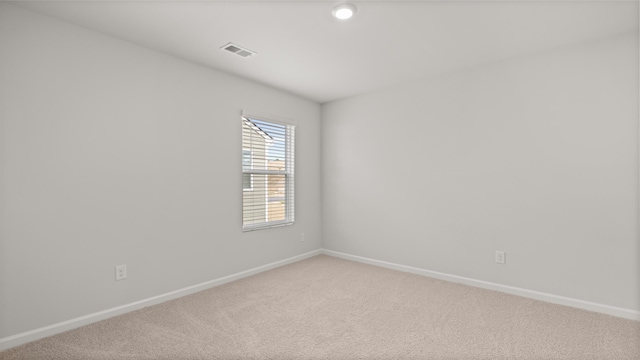 spare room featuring light colored carpet, visible vents, and baseboards