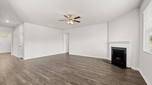 unfurnished living room featuring baseboards, a warm lit fireplace, ceiling fan, and dark wood-style flooring