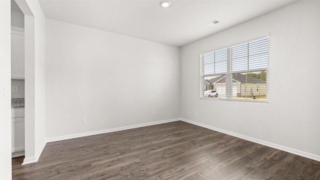 unfurnished room featuring dark wood finished floors, visible vents, and baseboards