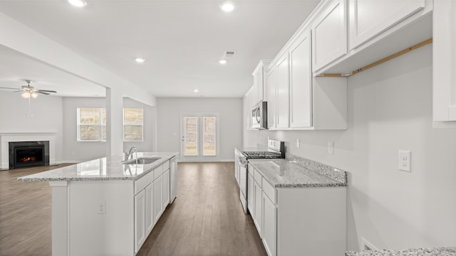 kitchen with white cabinets, a warm lit fireplace, stainless steel appliances, and wood finished floors