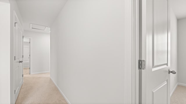 hallway featuring light carpet, attic access, and baseboards