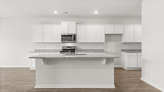 kitchen featuring a kitchen island with sink, a sink, white cabinetry, stainless steel appliances, and light stone countertops