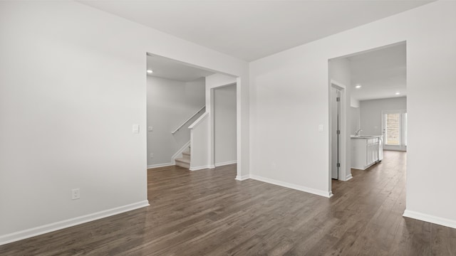 empty room featuring a sink, dark wood finished floors, recessed lighting, baseboards, and stairs